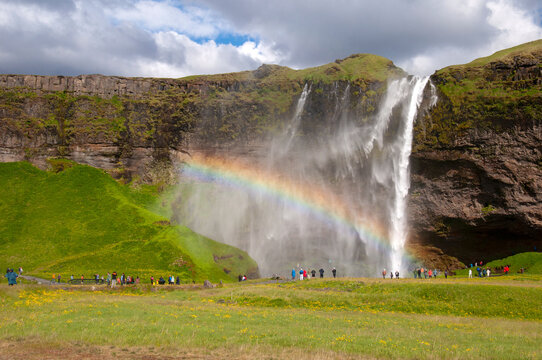 Seljalandsfoss Iceland, people sightseeing at waterfall with rainbow on a windy day