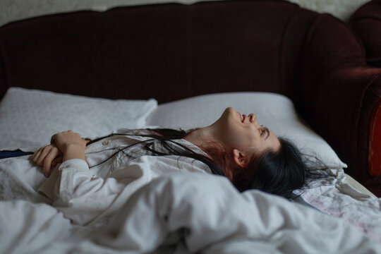 Woman in shirt lying on sofa bed at home looking up