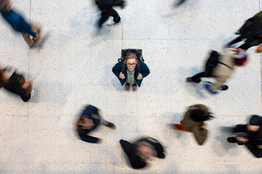 Commuter woman with backpack standing still amid rushing crowd overhead