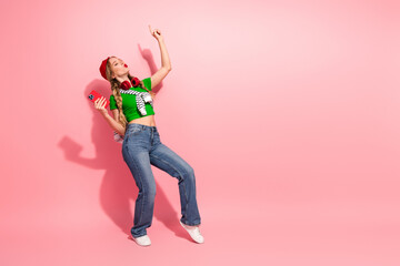 Young woman dancing against a pink background wearing a green top jeans and headphones