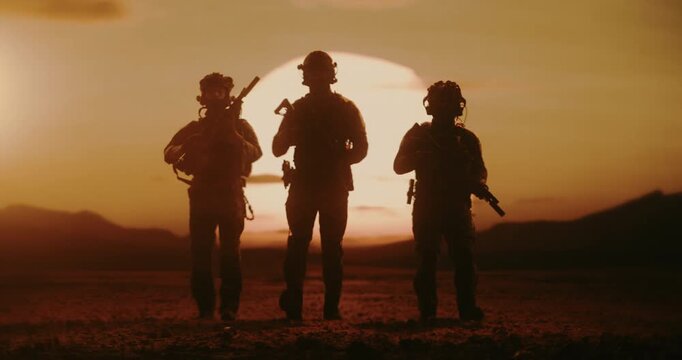 Silhouette of Armed Army Soldiers Walk Across a Desert at Sunset as Military Helicopter Flying in Background. Special Forces on War Mission, Warfare, Conflict. Cinematic Slow Motion Wide Shot