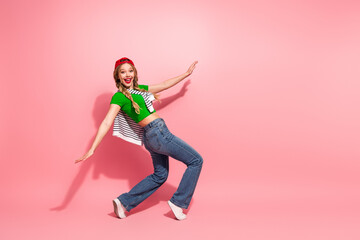 Young woman in green top jeans and cap dancing against pink background with striped cape smiling...