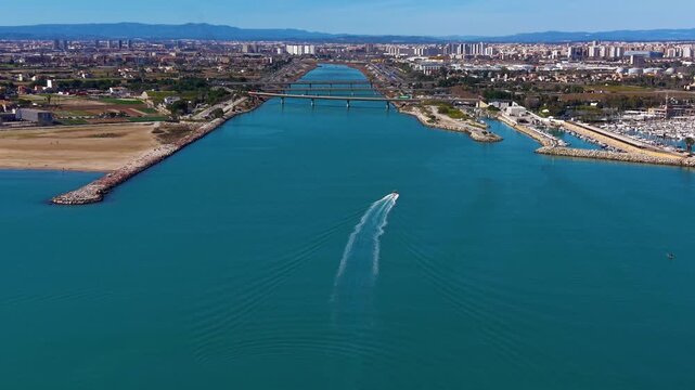 Aerial view of the Turia river channel flowing toward the Mediterranean Sea near Valencia, with bridges, marina infrastructure and urban skyline visible along the coastal waterway