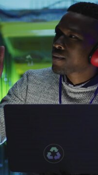 Tech dev sitting at laptop in green lab, raising finger, calling CO2 overlays while debugging code