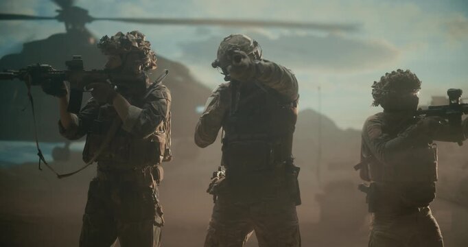 Three Male Special Forces Soldiers Advance From a Helicopter Landing in Desert War Zone, Weapons Ready, Executing a High Tech Combat Operation for Strike Warfare Support. Cinematic Action of Military
