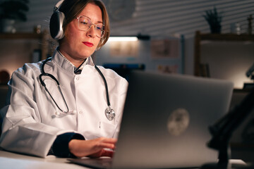 woman doctor working during night shift online using laptop computer. Telemedicine and emergency services © Andrii Lysenko
