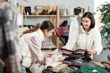 Seasonal trade sale, customer review at products in store and pick out clothes. Woman with child...