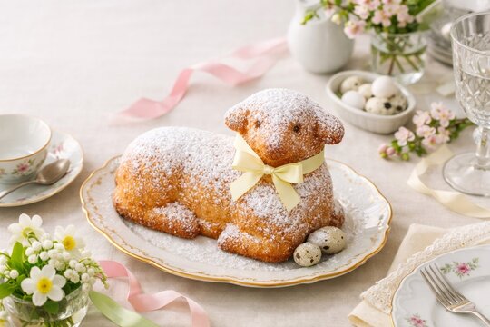 Traditional Easter lamb cake dusted with icing sugar and decorated with a yellow ribbon in a bright elegant style with white and pink colors symbolizing spring renewal copy space