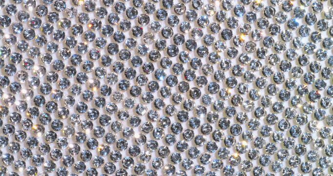 Rotating Sparkling Rhinestone. Macro video of faceted crystals sparkling intensely with smooth rotational camera movement on white surface.