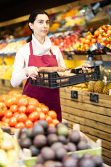 Obraz premium Young woman seller in apron offers cassava in box in vegetable shop