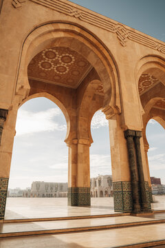 View of ornate arches framing a sun-drenched plaza, where the geometric patterns dance in the light, contrasting with the distant buildings, Casablanca, Casablanca-Settat, Morocco.