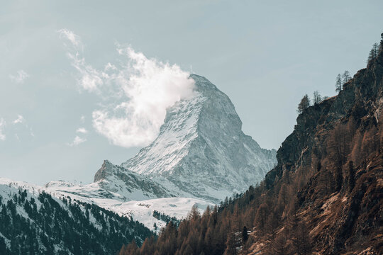 View of the iconic Matterhorn peak piercing the sky, its snow-dusted slopes contrasting with the rugged, tree-lined mountainside, Zermatt, Switzerland.