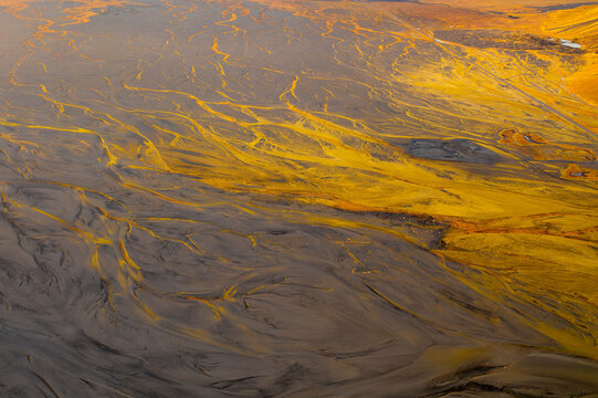 Aerial view of stark, contrasting textures paint the landscape with veins of bright yellow cutting through the muted earth tones, creating a surreal and captivating scene, Iceland.