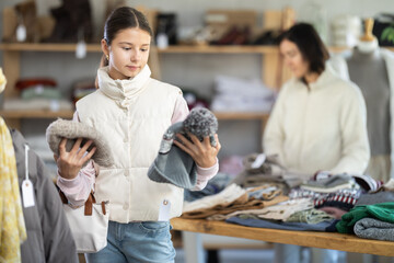 Teenage girl buyer choosing warm winter hat in clothing store