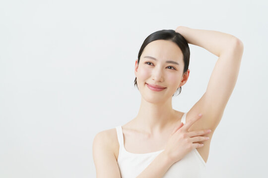白背景の脇に手を当てて微笑む若い日本人女性　脱毛イメージ