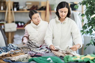 While shopping, mother and teen daughter looks at products in store and selects knitted jumper....
