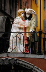 Venice, Italy - February 10, 2026: Two elegantly dressed individuals in ornate masks and costumes stand on a bridge during the Venice Carnival, showcasing intricate details and vibrant colors