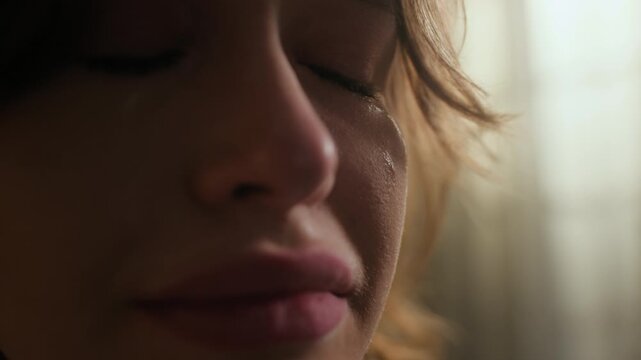 Extreme close up shot of young Caucasian woman weeping listening to music in wired earphones indoors