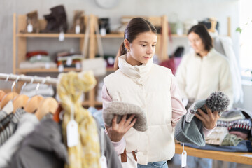 Teenage girl buyer choosing warm winter hat in clothing store