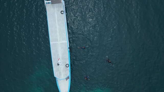 Aerial view of a boat at Cemara Kecil Snorkeling Spot, surrounded by the dark blue sea where people are snorkeling, Karimunjawa, Central Java, Indonesia.