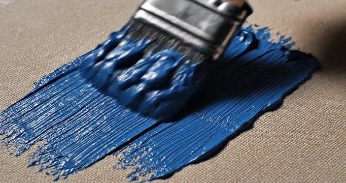 Close-up of a paintbrush applying vibrant blue paint on a textured canvas surface