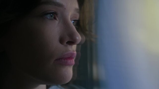 Zoom in handheld motion blur of listless Caucasian female zoomer standing by window with flickering light and contemplating at night