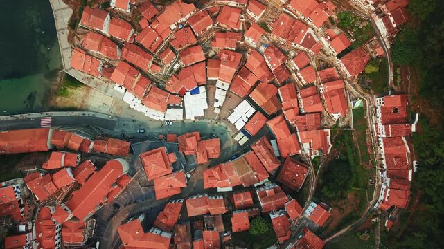 Top down rotating drone shot rising above Cudillero in Asturias revealing circular red rooftops and village layout.