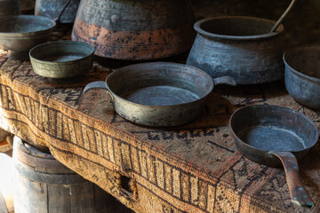 Fototapeta premium Worn antique metal pans and pots arranged on a patterned woven tablecloth create a rustic vintage kitchen atmosphere, evoking history, craftsmanship and traditional cooking utensils