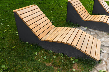 Modern wooden lounge benches set on green grass in a park, providing comfortable outdoor seating for relaxation, reading, sunbathing, and socializing in a landscaped garden or public space © evannovostro