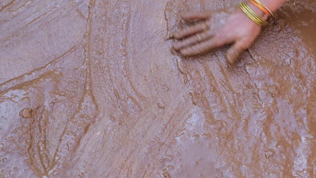 Hand with bangles applying wet mud coating on rural floor