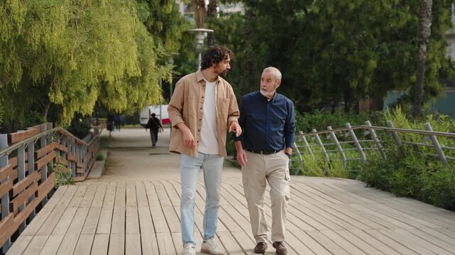Father and adult son walking talking sharing advice life conversation park outdoor