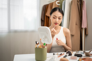 Young woman applying lip gloss and smiling in mirror. Beauty makeup routine with lipstick, lip...