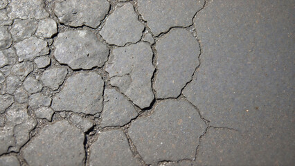 Fototapeta premium Extreme wear and tear visible on a deteriorating dark grey surface, exhibiting widespread cracking and rough texture