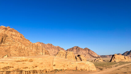 Desert landscape featuring rugged sandstone formations under a clear blue sky with distant...