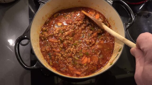 Stockholm, Sweden A cook stirs a Bolognese meat sauce with a wooden spoon. 