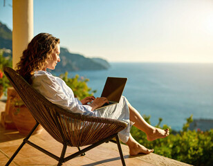 Fototapeta premium A woman enjoys the ultimate remote work lifestyle, using her laptop on a tranquil, sundrenched balcony overlooking the sea. Perfect for themes of freedom, luxury travel, and digital nomadism.