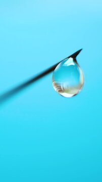 Fine point hypodermic needle with suspended drop of transparent fluid. Sterile injection device on blue background. Concept of pharmaceutical applications, disease prevention, medical precision