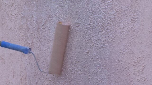 Pink paint covers rough surface of wall, bringing touch of modernity and warmth to newly constructed building. Simple tool completes process, contributing to projects overall progress