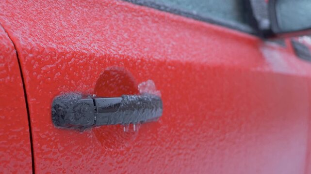 Black car handle on red vehicle encased in ice with icicles hanging. Handle is frozen solid freezing temperatures, difficult to open car door. Extreme cold can freeze car parts, causing inconvenience