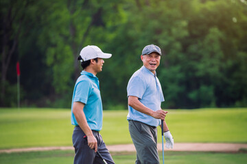 Senior golfer smiling while walking with younger partner on golf course fairway, active retirement lifestyle and outdoor sport recreation concept
