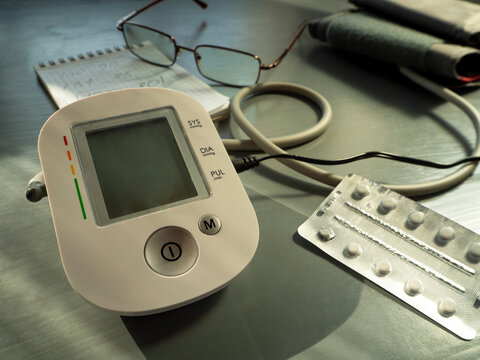A tonometer for measuring blood pressure, a tablet in a blister, glasses and a notepad are located on the table. Blood pressure control, prevention and treatment of hypertension.
