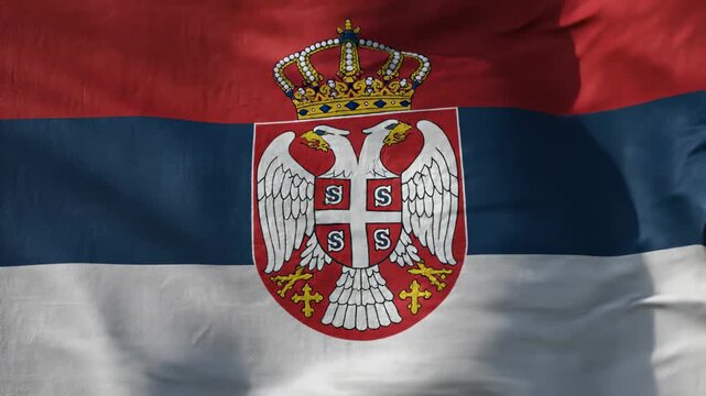 A close-up shot of the national flag of Serbia, featuring its red, blue, and white tricolor and the prominent double-headed eagle coat of arms with a crown.