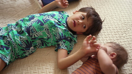 Naklejka premium Young boy lying on mat, looking at baby reaching out, gentle sibling interaction, childhood bonding, early family relationship, warm and affectionate moment