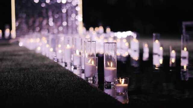 Rows of glowing candles in glass holders lighting wedding aisle at night