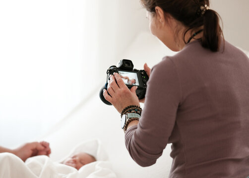 Woman Takes Pictures Of Newborn Baby While Mom Holds Baby Hand. Bright And Warm Setting.