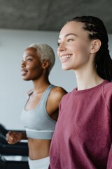 Obraz premium Smiling young caucasian female and young african female on treadmills in gym young adult fitness workout together