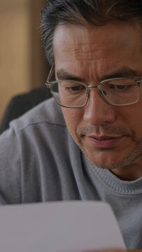 Middle-aged man lifting paper and reading, frowning then relaxing while reviewing business document