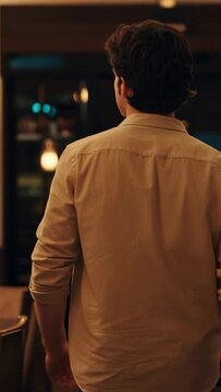 Vertical video: Stepping away from service counter, man in beige shirt walking under pendant lights