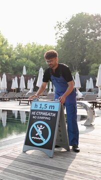 Employee carrying a safety sign with depth and no jumping rule by the swimming pool, ensuring guest safety at resort