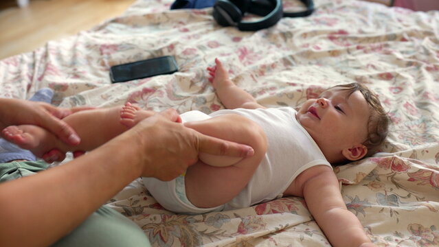 Mother performing bicycle leg movements on baby to relieve gas, joyful moment, infant care, soothing technique, digestion relief, sensory interaction, comfort, family bond